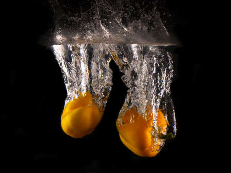 yellow Bell pepper falling into splashing water on black backgroundの写真素材