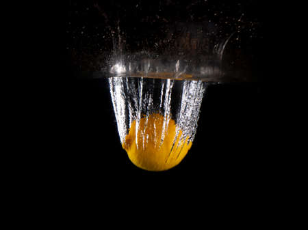 yellow lemon falling into splashing water on black backgroundの写真素材
