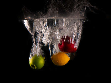 green and red apple , yellow lemon falling into splashing water on black backgroundの写真素材
