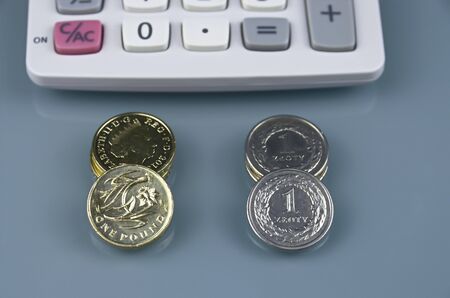 One pound and polish zloty coins on grey background against calculatorの写真素材