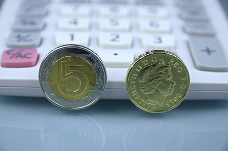 One pound and polish zloty coins on grey background against calculatorの写真素材