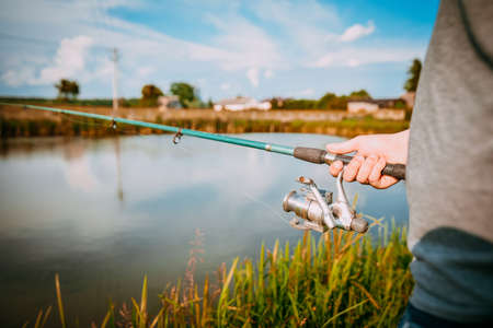 Young man fishing on lake at sunset enjoying hobby. Outdoor, activity. Narrow focus.の写真素材