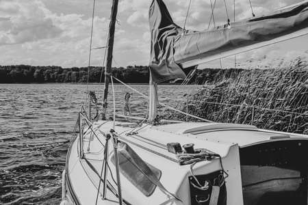 White motor or sail boat anchored on the lake pier or dock with green river reeds, black and white
