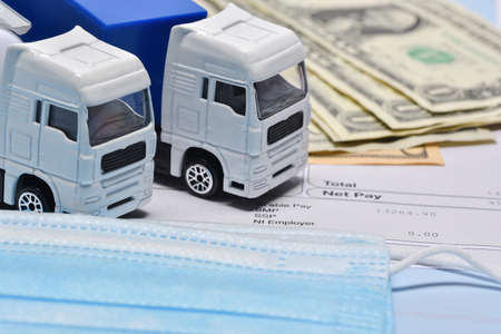 A lorry toys, payroll with dollar bill and face mask in concept about transport departament against coronavirus pandemic.の写真素材