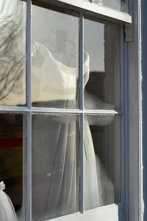 Old white wedding dress on display in an old shopping windowの写真素材