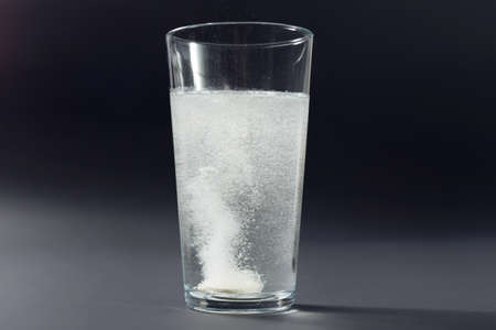 Soluble pill tablet in water with bubbles on black contrasty background