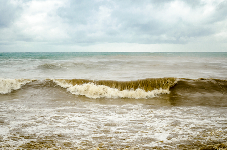 Stormy sea with brown water and foamy waves under thick blue cloudsの写真素材