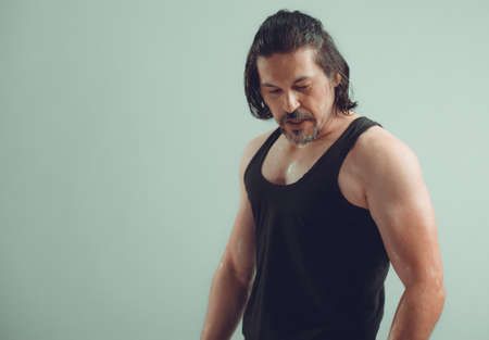 Male bodybuilder wearing dark tanktop on ripped muscular torso in studio shotの写真素材