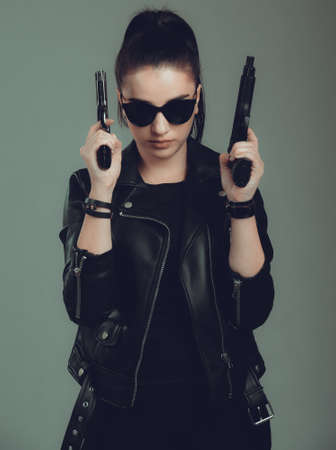 Shot of a   military woman posing with guns,in a black jacket,black glasses in the eyesの写真素材