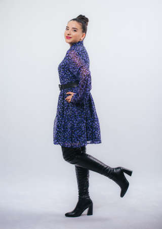 Happy beautiful woman in blue dress posing in studio isolated on white background,black long boots on his feet, Full length portrait,の写真素材