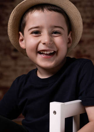child on chair smiling on his face brick wall backgroundの写真素材