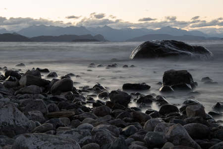 a large smooth stone in the water on the lake shore against the background of mountains is a long exposition. San Carlos de Bariloche, Argentinaの写真素材