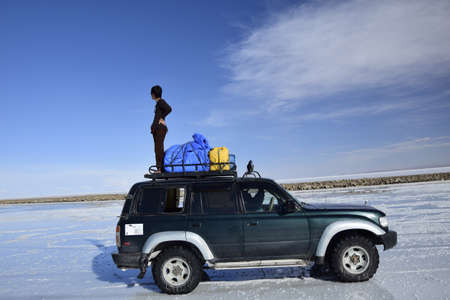 A tourist is standing in a car, in the middle of Salar de Uyuni, Bolivia