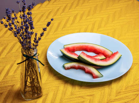slices of watermelon on a plate with a sprig of lavender in a vaseの写真素材