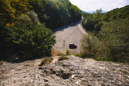 Jumping man, standing next to a red car. Shot from above