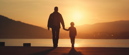 Silhouette of father and son walking on pier at sunset.の素材