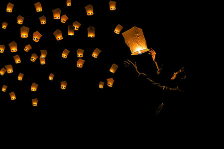 A person in darkness holding a lantern, illuminating the immediate area. The light from the lantern casts shadows, revealing minimal details of the surrounding environment.の素材