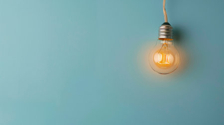 A light bulb is suspended from the side of a wall, casting a bright glow in the surrounding area. The bulb is securely attached to the wall with wires, providing illumination to the space.の素材