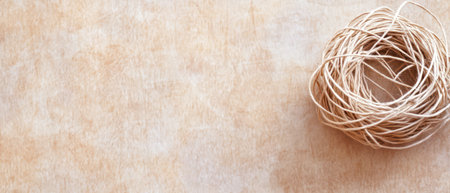 A neatly coiled bundle of natural twine rests on a textured wooden surface, reflecting soft daylight. The warm tones enhance the rustic charm of the setting, creating an inviting atmosphere.の素材