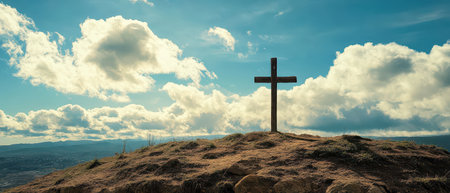 A wooden cross stands on a grassy hill under a vast sky filled with clouds during daylight. The scenery captures tranquility and reflection.の素材