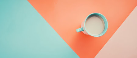 A turquoise mug filled with milk sits on a vibrant geometric backdrop of orange and blue colors creating a minimalist aesthetic.の素材