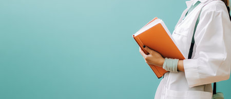 A health worker stands by a turquoise wall holding an orange notebook while wearing a white coat and stethoscope ready for appointments.の素材