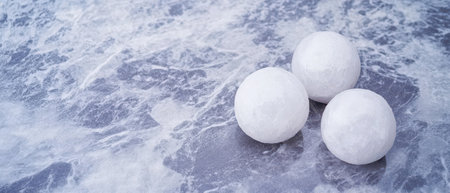 Three white spherical objects are placed on a smooth gray surface creating a minimalist aesthetic with subtle texture.の素材