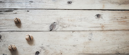 Three walnuts rest on a weathered wooden table showcasing their textured shells and natural colors in a serene rustic setting.の素材