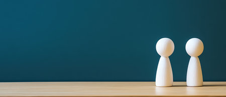 Two minimalist wooden figures stand close together on a light wooden surface against a dark blue wall in a calm and serene environment.の素材
