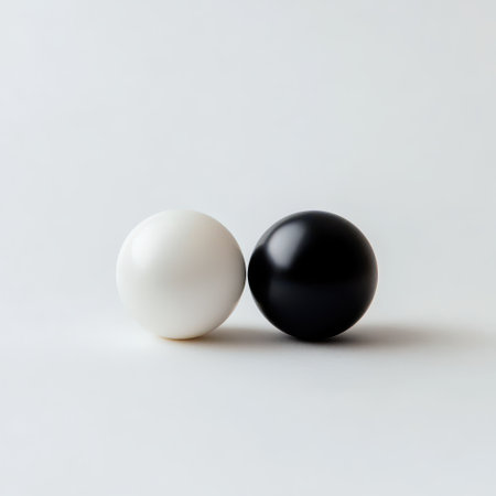 Two smooth spheres one black and one white rest closely on a minimalistic background highlighting their contrasting colors and shapes.の素材