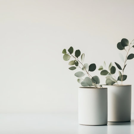 Two white pots showcase delicate eucalyptus branches bringing a touch of nature and elegance to a simple clean setting.の素材