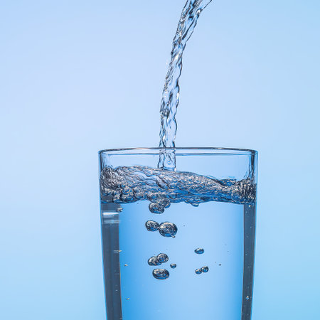 Fresh water is being poured into a glass producing bubbles as it fills up. The background is a soft blue enhancing the refreshing feel.の素材