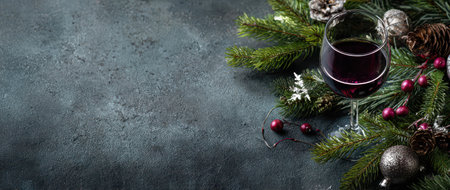 A festive glass of red wine rests among pine branches and holiday decor setting the mood for a warm New Year celebration.の素材