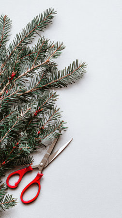 Fresh pine branches and red scissors are arranged on a light backdrop perfect for crafting holiday decorations and New Year celebrations.の素材