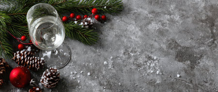 Sparkling wine glass rests on a holiday themed table surrounded by pine branches red ornaments and winter decor for New Year celebration.の素材
