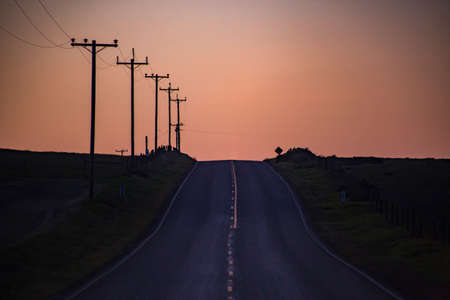 The road and Electrical lines show an orange sky at dawnの写真素材