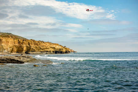 US coastguard helicopter in flight, Point Loma Beach. US coastguard helicopter in flight with a person hanging after someone fell off a cliffの写真素材