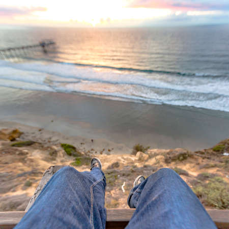 Legs hanging off the edge of a building with the ocean and pier views of the sunset . Southern California coastal viewsの写真素材