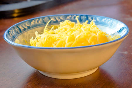 Grated mozzarella and cheddar cheese in dish over wood. Grated mozzarella and cheddar cheese in white and blue bowl over wooden backgroundの写真素材