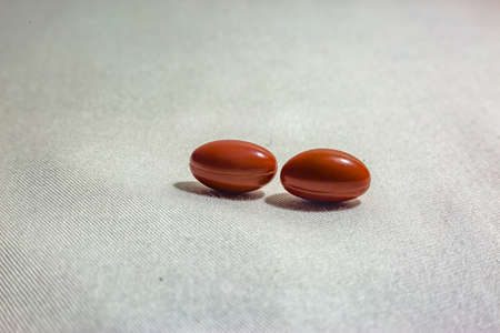 Double pills on a white background with fabric texture shot in studio. Orange or red pills on a textured white backgroundの写真素材
