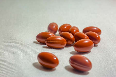 Group of pills with two in the foreground on a white background with fabric texture shot in studio. Orange or red pills on a textured white backgroundの写真素材