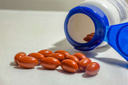Pills and opened bottle on a white background with fabric texture shot in studio. Orange or red pills with open bottle on a textured white backgroundの写真素材