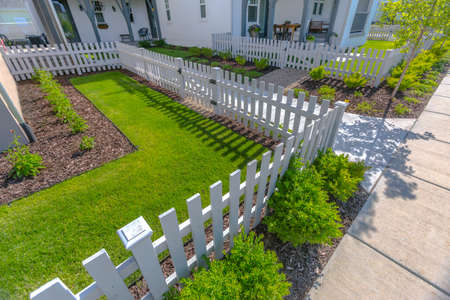 Front yard with lawns and shrubs with white fenceの写真素材
