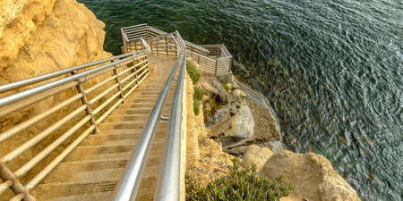 Sunlit stairs on a cliff going down the calm ocean