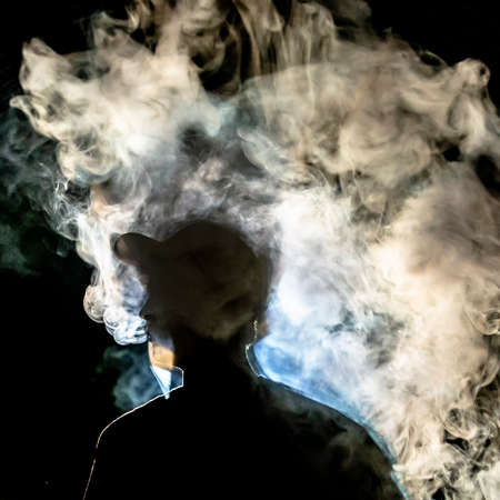 Man with smoke silhouetted against dark background