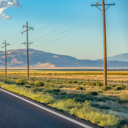 Power lines on grassland against mountain and skyの写真素材
