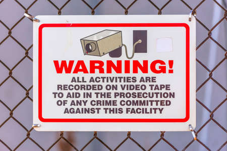 Warning security camera sign on a chain link fence