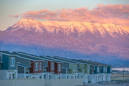 Homes against Mount Timpanogos lit by setting sun. Row of homes in Utah with a view of the towering Mount Timpanogos under cloudy sky. The mountain is lit with a golden glow by the setting sun.の写真素材