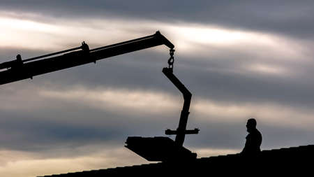 Silhouette of a crane and man on roof of homeの写真素材