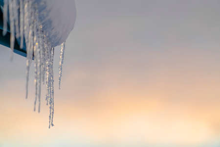 Pointed icicles hanging from a snow covered roofの写真素材